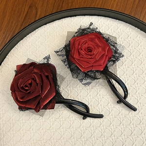 Elegant red satin rose flower hair clip with black lace trim on a textured tray