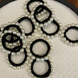Élastiques à cheveux noirs avec perles blanches présentés sur un plateau tressé
