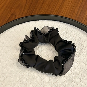 Elegant black satin and organza scrunchie with crystal beads on a textured white plate