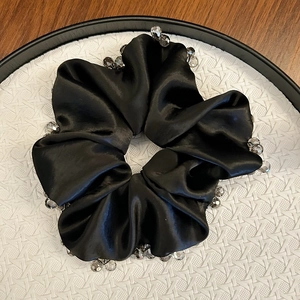 Detail of a black satin scrunchie with sparkling clear and gray beaded trim on a tray