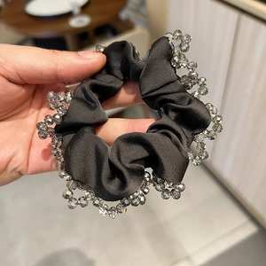Detailed view of black satin scrunchie with grey crystal beaded edges held by hand