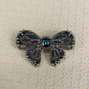 Detailed close-up of a luxury blue bow brooch with sparkling crystals and grey pearls