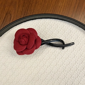 Detail of red velvet camellia flower on a black hair clip with textured background