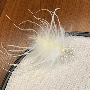 Close-up of white feather hair clip featuring elegant faux pearls and woven base detail