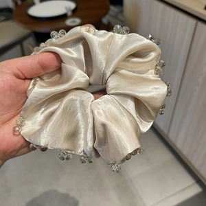 Detail of champagne satin scrunchie featuring luxury faceted crystal bead edges