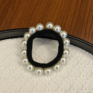 Élastique à cheveux noir avec perles blanches élégantes posé sur un plateau tressé