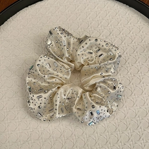 Gros plan du chouchou en satin champagne serti de strass sur un plateau blanc