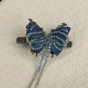 Dettaglio di un fermaglio per capelli a farfalla blu ricamato con perle e nappe