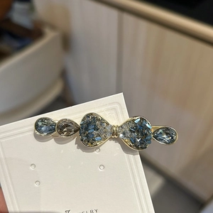 Close-up of crystal bow hair clip with blue gemstones and gold alloy setting on card