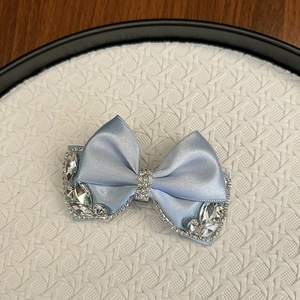 Detailed macro of light blue satin bow hair clip featuring sparkling rhinestone borders