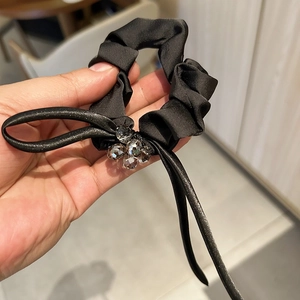 Detailed view of black satin hair scrunchie with crystal flower and long ribbon tie
