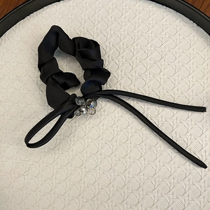 Detail of black satin scrunchie with crystal beads and long ribbons on a white tray