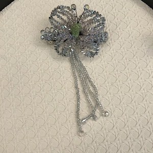 Detailed macro view of handmade beaded butterfly hair clip with green accents and tassel drops