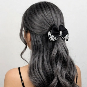 Close-up of black satin bow hair clip with sparkling rhinestones on grey curly hair