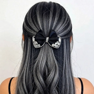 Macro shot of a black satin bow hair clip featuring sparkling rhinestones on long dark hair