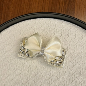 Macro shot of off-white satin bow hair clip with luxury rhinestones and crystal details