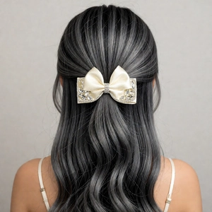 Detailed back view of a creamy satin bow hair clip with sparkling rhinestones on wavy hair