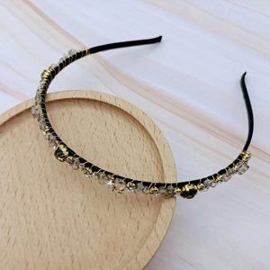 Detail of black headband with gold wire, green and clear crystals on marble background