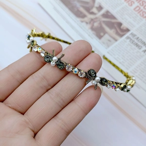 Detailed close-up of a gold metal headband with green crystals and white pearls