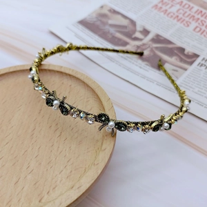 Detailed close-up of retro headband with green gemstones and white pearls on gold base