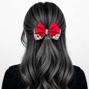 Detail of a red satin bow hair clip with sparkling rhinestones on grey wavy hair