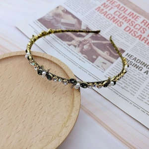 Detailed close-up of a gold metal headband with pearls, green rhinestones and a bow