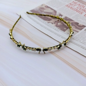 Close-up of golden headband with green rhinestones and white pearls on vintage paper