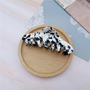 Detail view of large marble pattern hair claw clip on wooden plate and stone surface