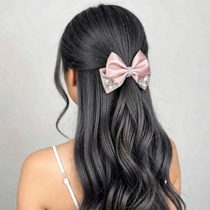 Detail of pink satin bow hair clip with sparkling rhinestones worn on wavy hair