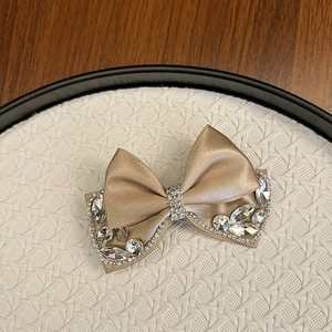Detail of champagne satin bow hair clip with sparkling rhinestones and crystal accents