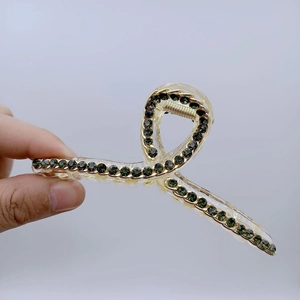 Dettaglio della grande pinza per capelli con strass verdi e catena in metallo dorato