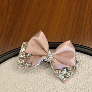 Detailed close-up of pink satin bow hair clip with sparkling rhinestones on a white tray