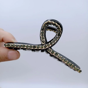Dettaglio della grande clip per capelli nera con catena dorata e strass verdi brillanti