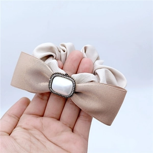 Détail du chouchou nœud perlé avec strass étincelants et tissu plissé beige élégant
