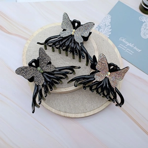 Set of three butterfly rhinestone hair claws in black on a wooden tray for elegant styling