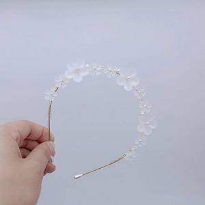 Détail d'un serre-tête floral avec fleurs mates blanches et perles sur monture dorée fine