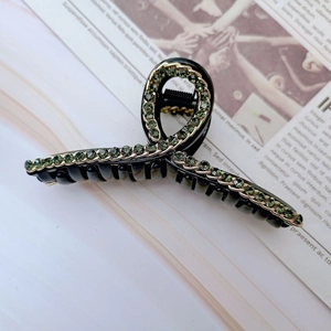 Dettaglio di una grande pinza per capelli nera con strass verde scuro e catena dorata