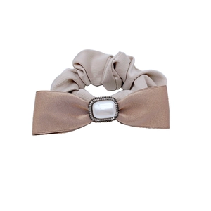 Chouchou satiné champagne élégant avec nœud, perle et strass sur fond blanc immaculé