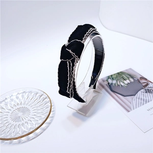 Detail of elegant black knit headband with white scalloped edge bow on white background
