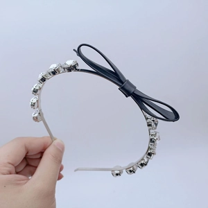 Détail d'un serre-tête en métal argenté avec de gros strass et un nœud en cuir noir élégant