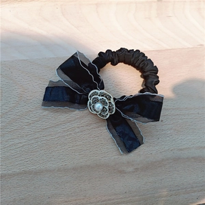 Detailed shot of black satin hair tie with rhinestone camellia and lace bow accent