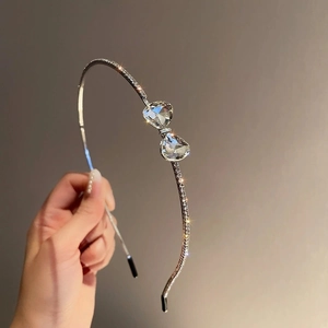 Macro detail of silver hairband showing shimmering rhinestone bow with heart-shaped crystals