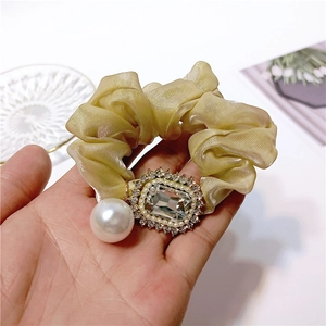 Detailed shot of champagne glitter scrunchie with large crystal and dangling white pearl