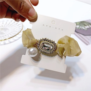Close-up of champagne gold pleated fabric hair scrunchie with rhinestones and large pearl