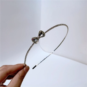 Close-up of a slim silver metal headband with a sparkling rhinestone bow detail