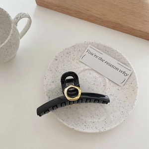 Elegante molletta per capelli grande in acrilico nero con anello dorato su piatto bianco