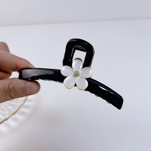 Détail d'une pince à cheveux noire ornée d'une fleur blanc nacré au centre doré