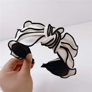 Detail view of cream pleated bow headband with black contrast piping craftsmanship