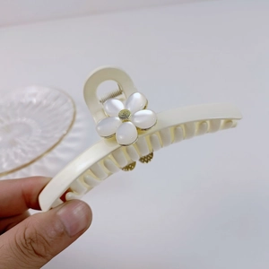 Détail d'une pince à cheveux crème avec motif floral blanc et fini œil-de-chat