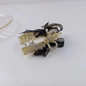 Détail de la pince à cheveux dorée avec nœud en organza noir et perles blanches
